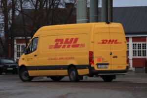Yellow DHL van on street showing company branding and delivery services.